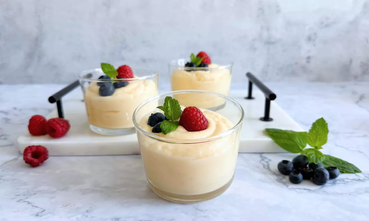 Helles Mousse au Chocolat in kleinen Gläsern, cremig aufgeschichtet, dekoriert mit Beeren und frischen Minzblättern auf Marmorplatte drapiert