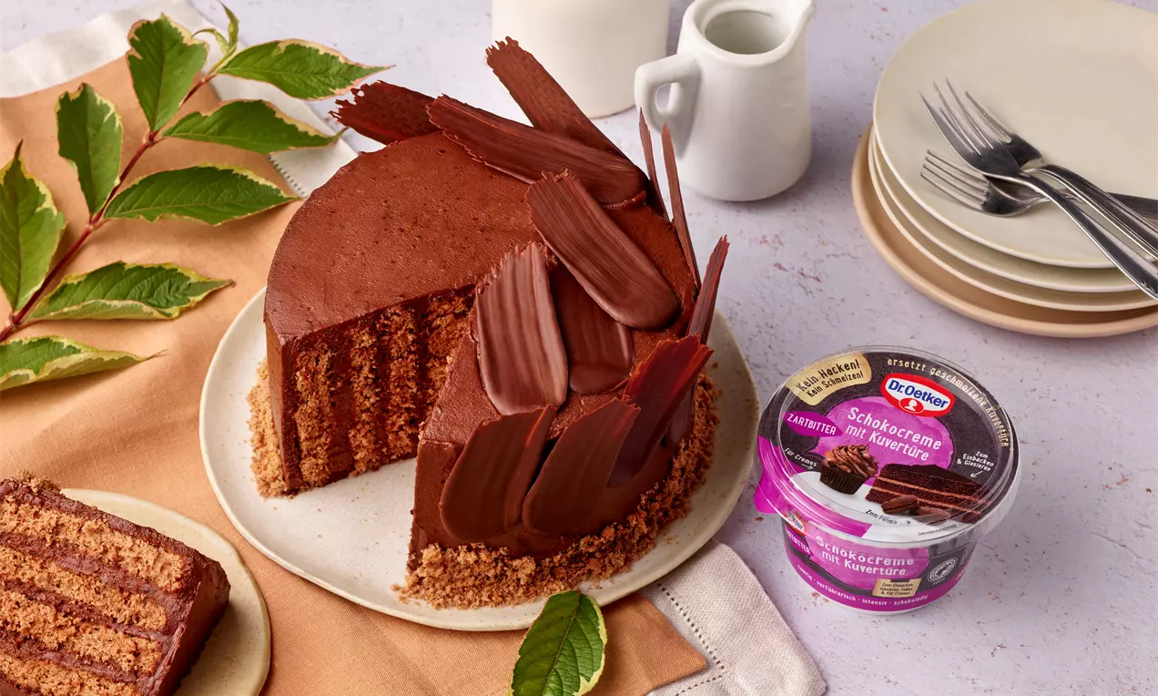 Schoko-Wickeltorte mit Schichten aus dunkler Creme und Biskuit, dekoriert mit Schokoladenspänen, auf einem Teller mit grünen Blättern