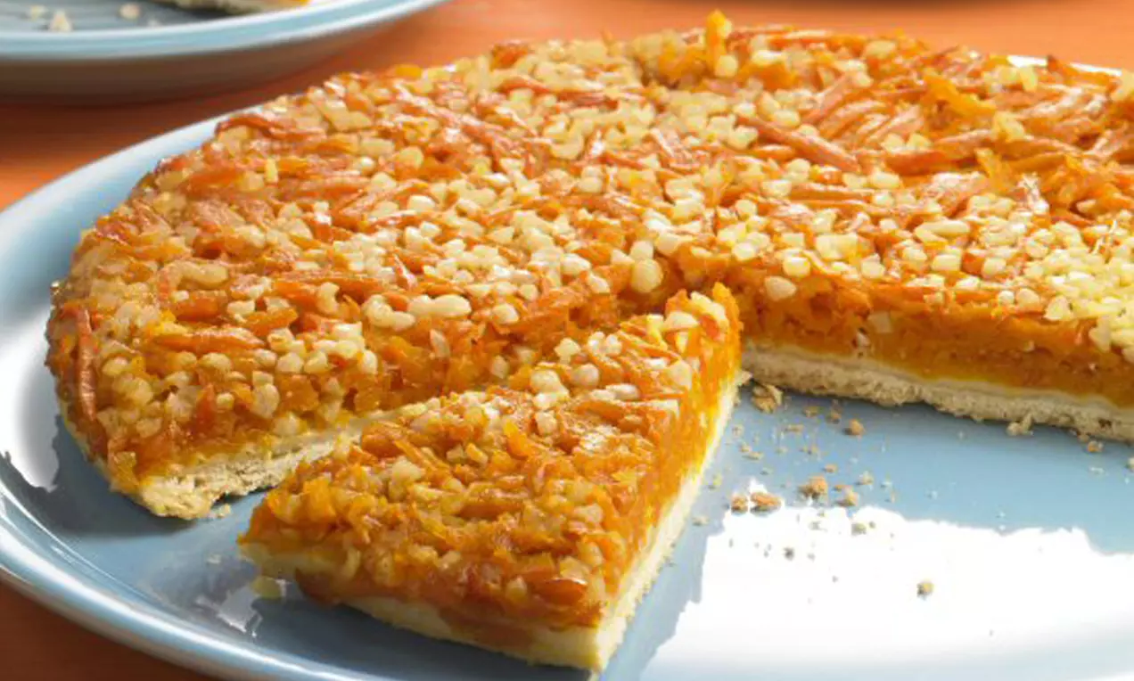 Goldene Kürbis-Tarte mit karamellisierten Nüssen auf einem hellblauen Teller, eine Ecke herausgeschnitten und daneben platziert