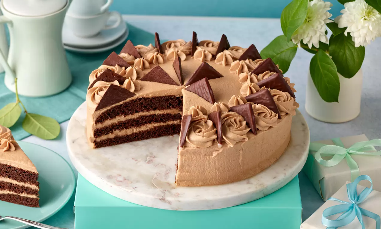 After-Eight®-Torte mit schokoladigen Böden, hellbrauner Creme und dunklen Schokoladendreiecken auf einem weißen Teller aus Marmor