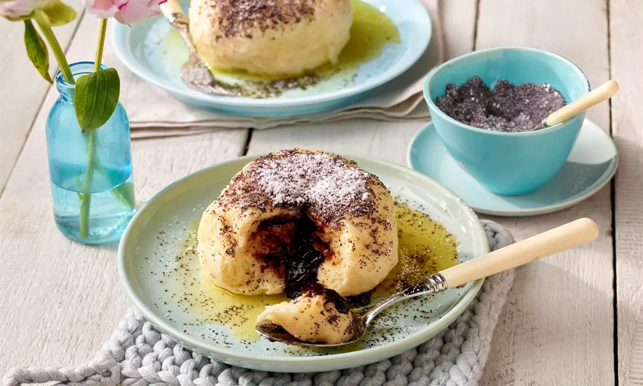 Germknödel mit heller, weicher Oberfläche, bestreut mit Mohn und Puderzucker, angerichtet auf einem Teller mit flüssiger Butter und aufgeschnitten