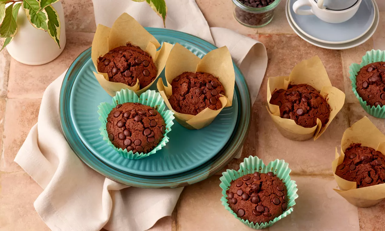 Schokoladenmuffins mit dunklem, feuchten Teig und glänzenden Schokotropfen in braunem und grünem Papier auf einem türkisfarbenen Teller