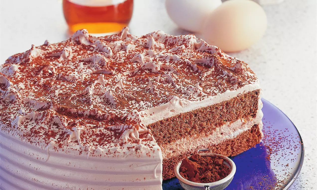 Zweischichtige Schaumtorte mit fluffigem Schokoladenboden und Creme, dekoriert mit Kakaopulver, serviert auf einer blauen Platte