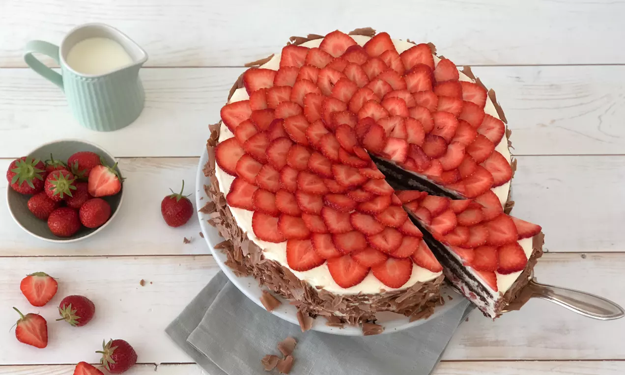 Schwarzwälder Erdbeertorte mit saftig roten Erdbeerscheiben in Rosettenform auf Sahneschicht, umrandet von Schokoraspeln auf weißem Teller