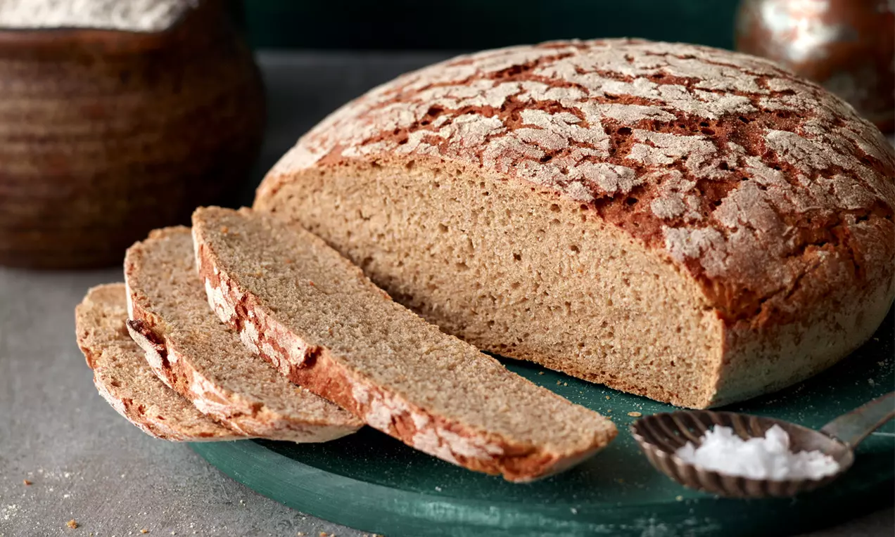 Rundes Mischbrot mit goldbrauner Kruste und heller Mehltextur, angeschnitten und in gleichmäßige Scheiben auf grünem Teller angerichtet