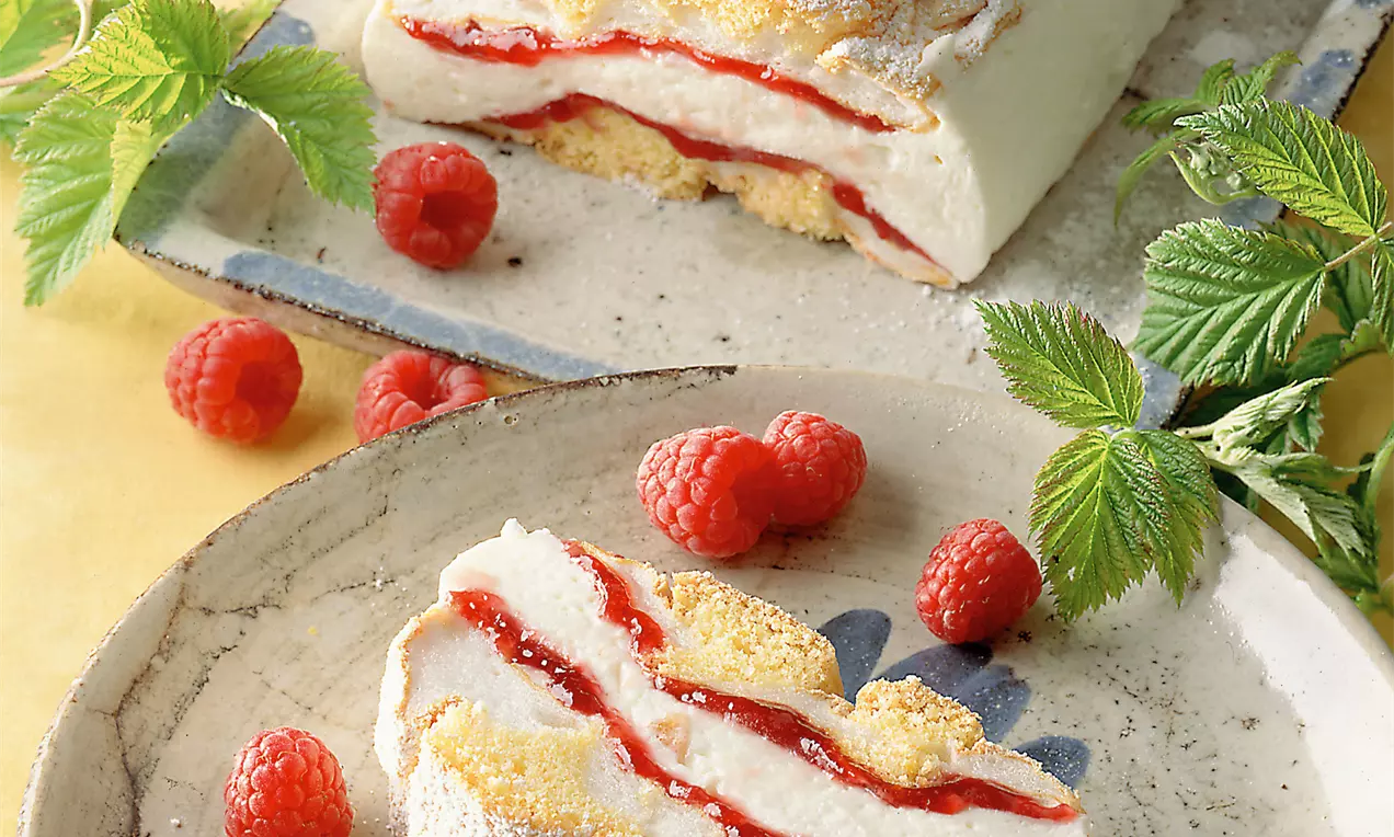 Kardinalschnitte mit luftiger Schaumcreme, heller Biskuitmasse, roter Marmeladenschicht, mit Puderzucker bestäubt auf rustikalem Teller mit Himbeeren