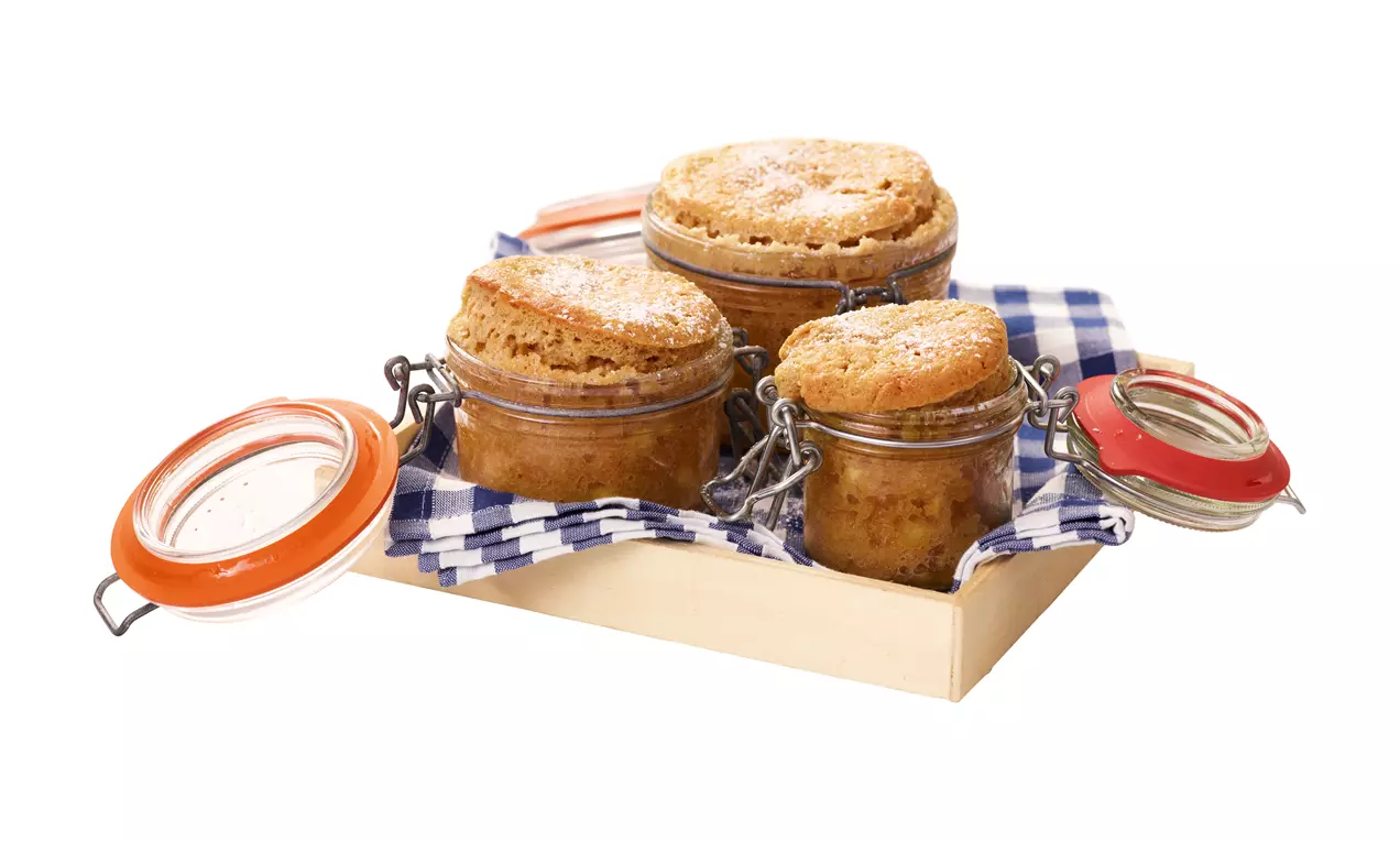 Apfelkuchen mit goldbrauner, knuspriger Kruste in bauchigen Gläsern mit Bügelverschluss auf kariertem Tuch in Holzkiste arrangiert