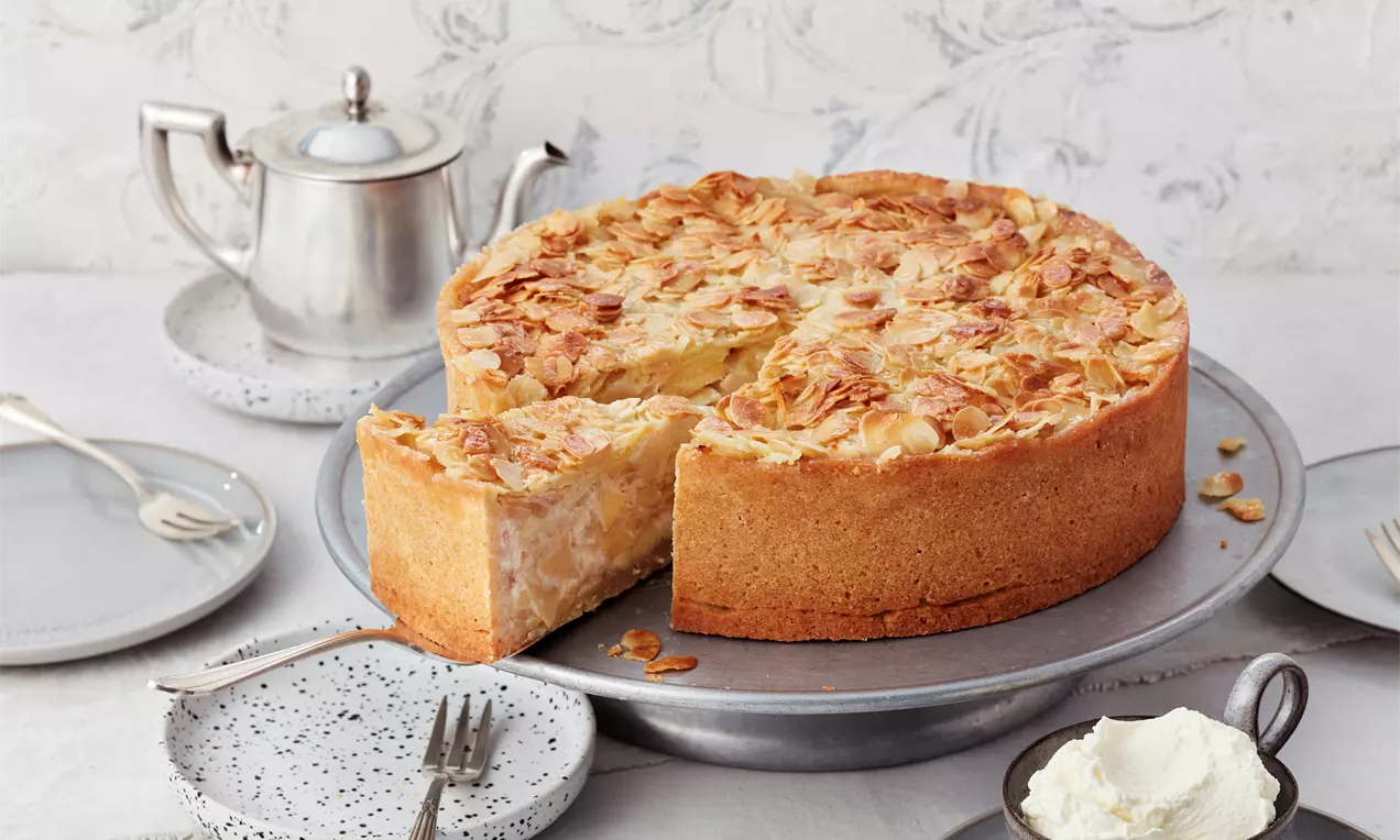 Goldbraune Apfel-Bienenstich-Torte mit knusprigen Mandelblättchen auf einer silbernen Tortenplatte, serviert mit Sahne und Teeservice