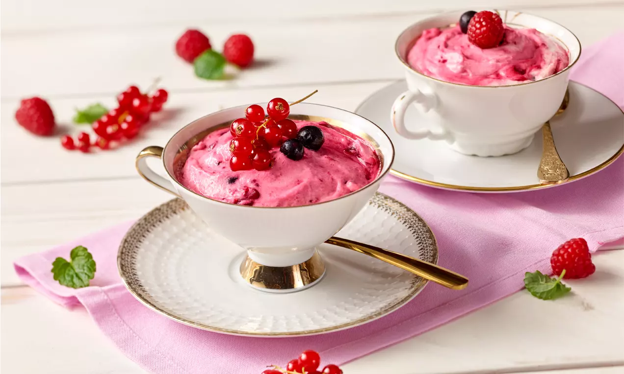 Sahnig rosa Creme mit leicht luftiger Textur in eleganten weißen Tassen, garniert mit roten Beeren und dunklen Johannisbeeren