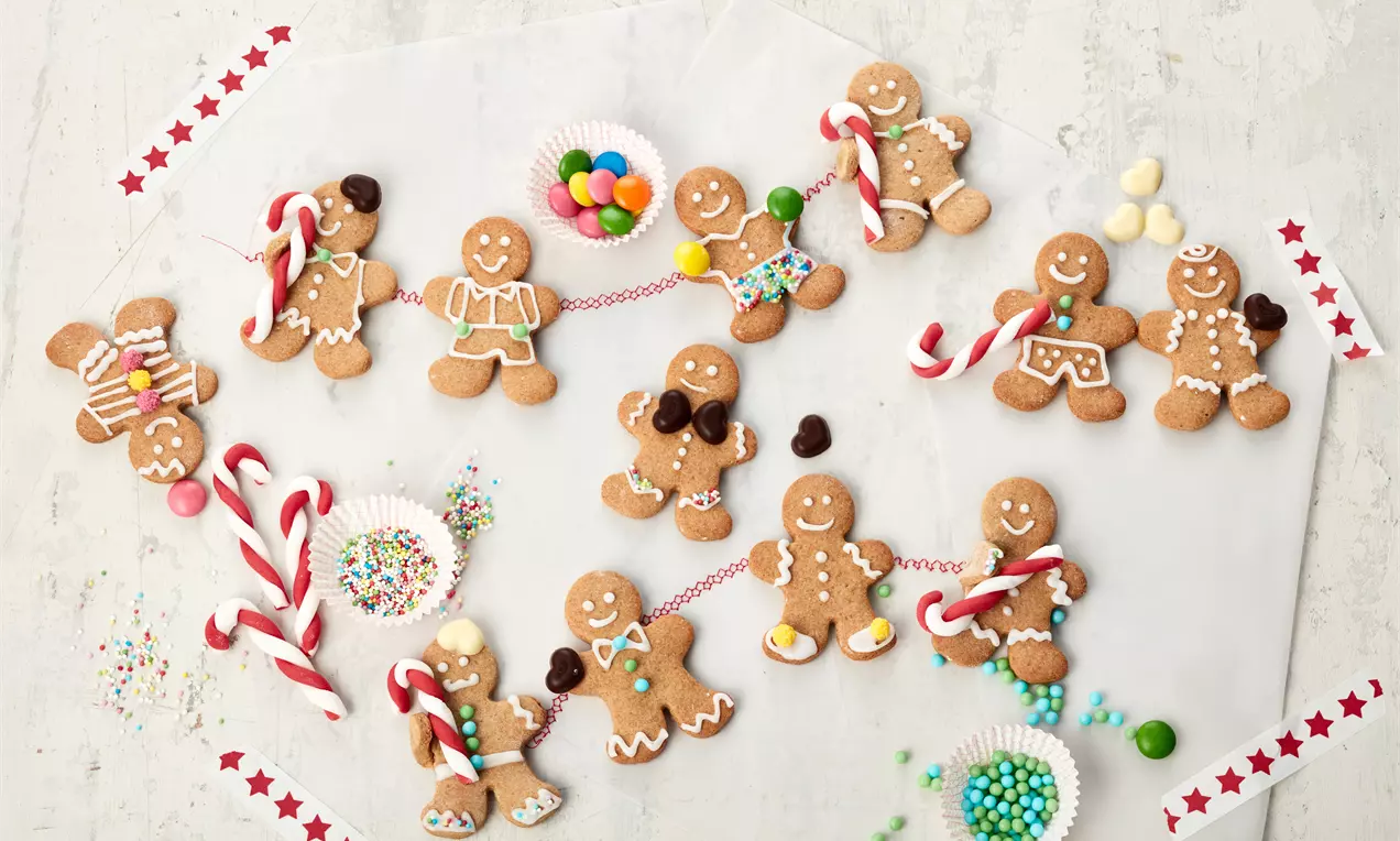 Lebkuchenmänner in warmem Braun, verziert mit buntem Zuckerguss und bunten Details, umgeben von Zuckerstangen und kleinen Süßigkeiten