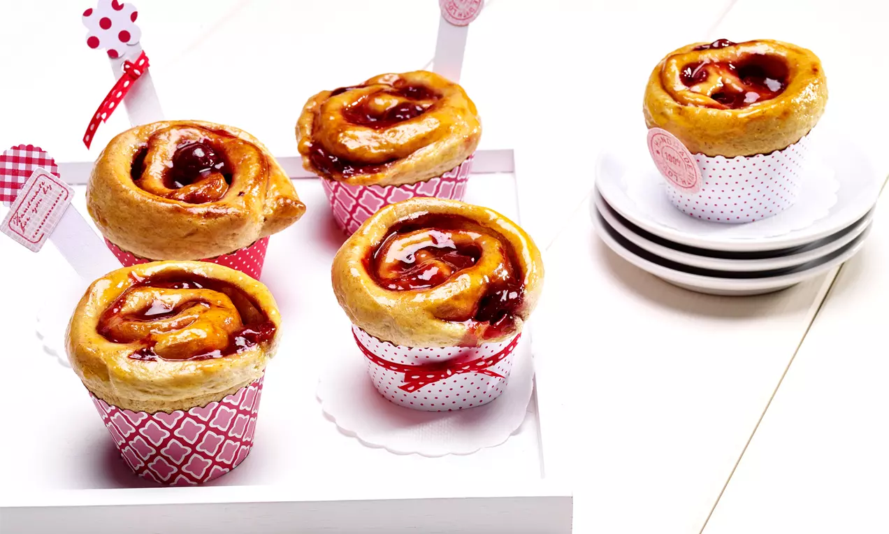 Goldene spiralförmige Kirsch-Rosen-Gebäcke mit glänzender Oberfläche, verpackt in roten und weißen Förmchen auf einem weißen Tablett