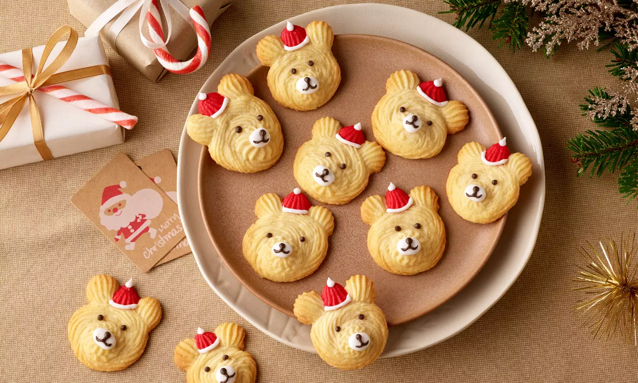 Plätzchen in Bärenform mit goldgelber Oberfläche und roten Zuckermützen, arrangiert auf einem runden Teller mit weihnachtlicher Dekoration