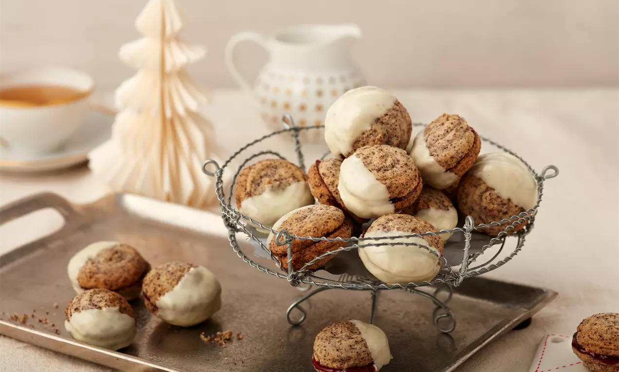 Gefüllte Mohnplätzchen mit braunen und weiß glasierten Hälften, kunstvoll auf einer filigranen Metall-Etagere drapiert vor weihnachtlicher Kulisse