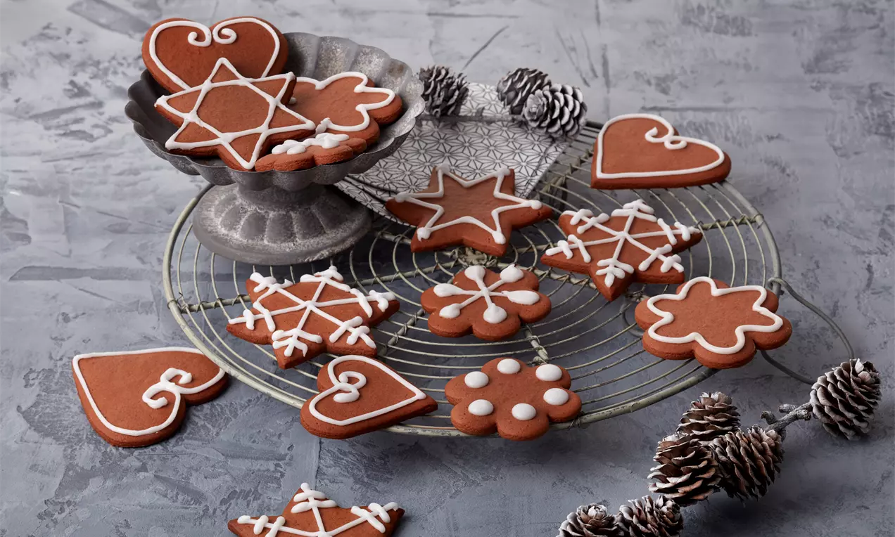 Lebkuchenplätzchen in verschiedenen Formen mit weißem Zuckerguss verziert, auf einem Gitter mit Zapfen und Metallständer arrangiert