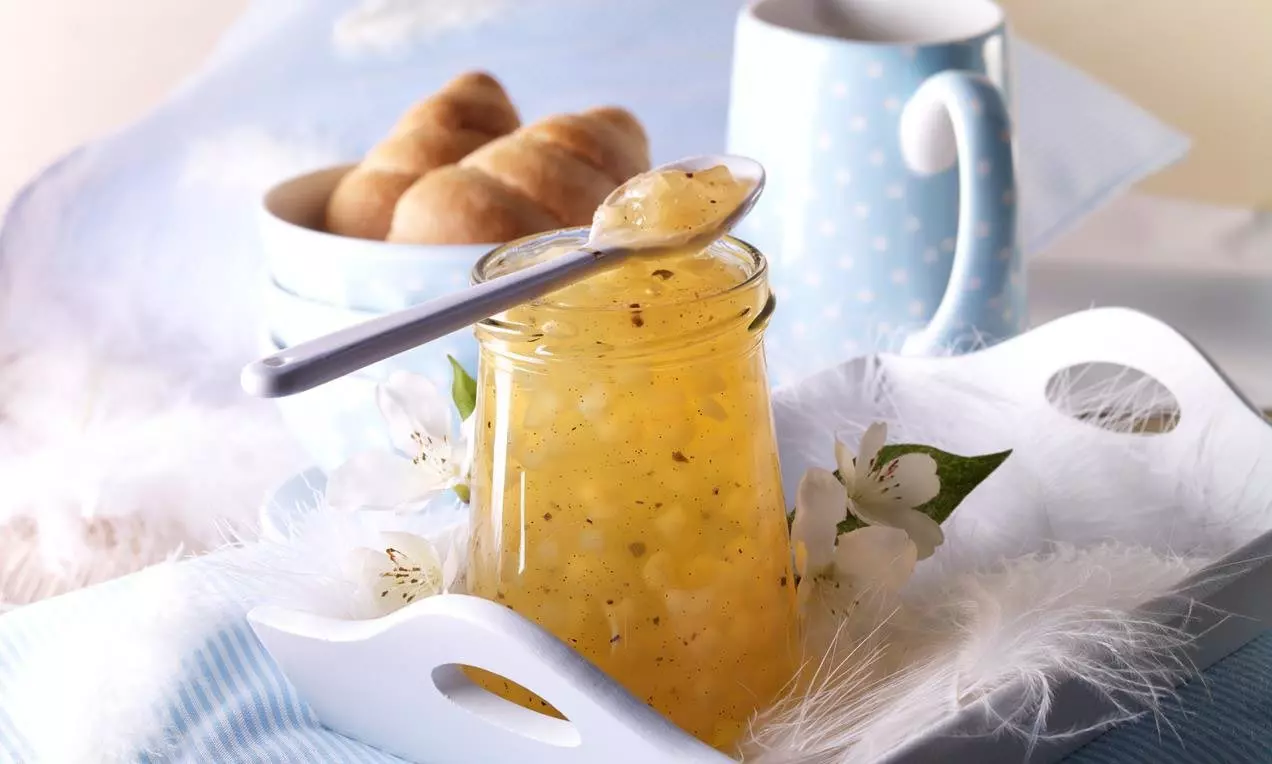 Honiggelbes Apfelgelee mit zarten Birnenstückchen in einem Glas, sanft dekoriert mit weißen Blüten und Federn auf einem Tablett