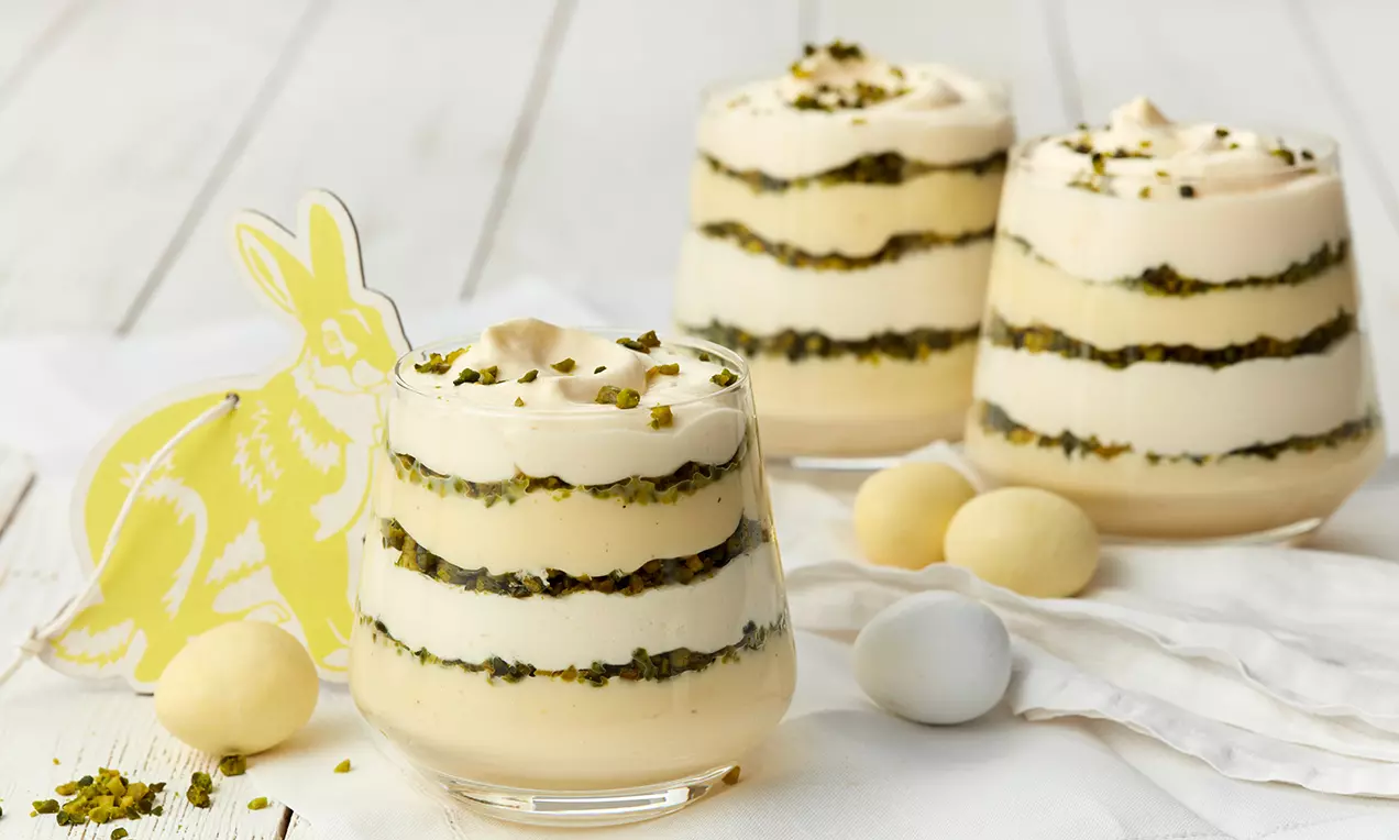 Mehrschichtige Gläser mit hellgelber Eierlikör-Creme, weißer Sahne und grünem Pistazienbruch, dekoriert mit Ostereiern und Papierhase