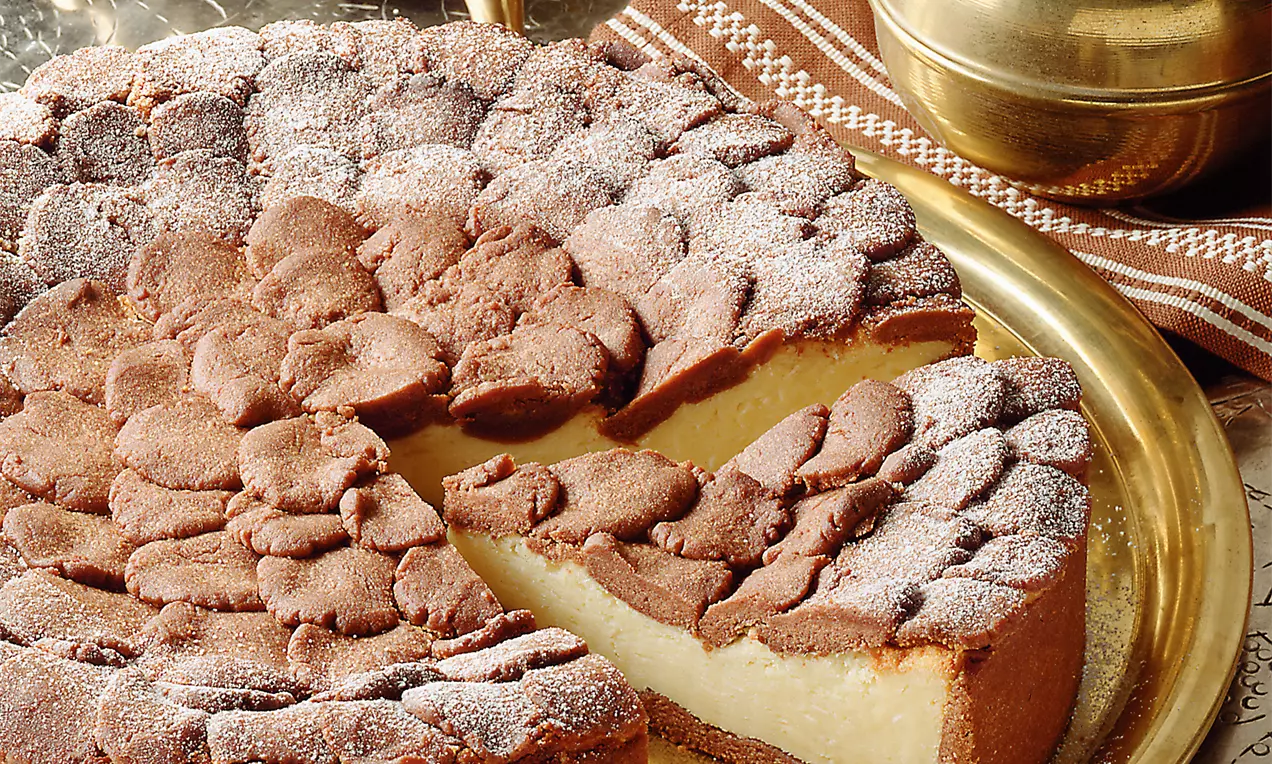 Russische Zupftorte mit dunkelbraunem Kakaoteig und zartgelber Füllung auf einem goldenen Teller, bestäubt mit Puderzucker, neben einem Samowar