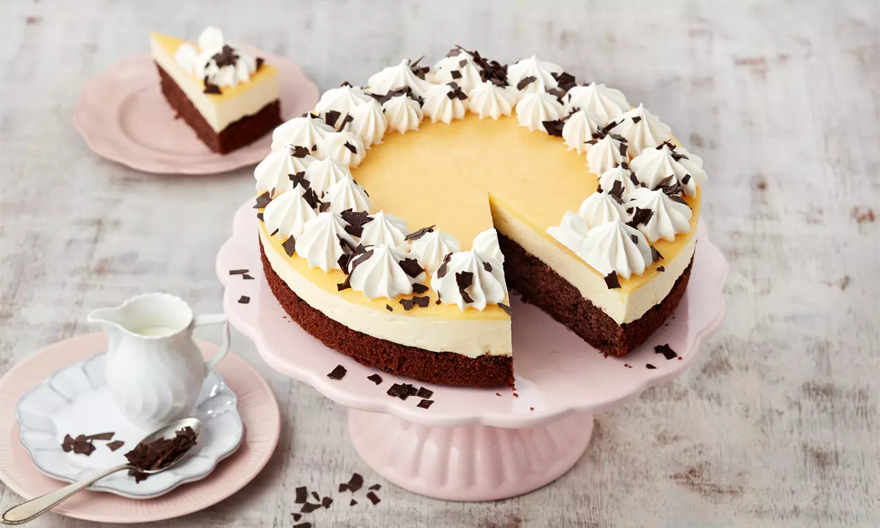 Eierlikörtorte mit gelber Creme, Sahnetupfen und Schokoraspeln auf dunklem Boden, angeschnitten auf rosafarbener Tortenplatte