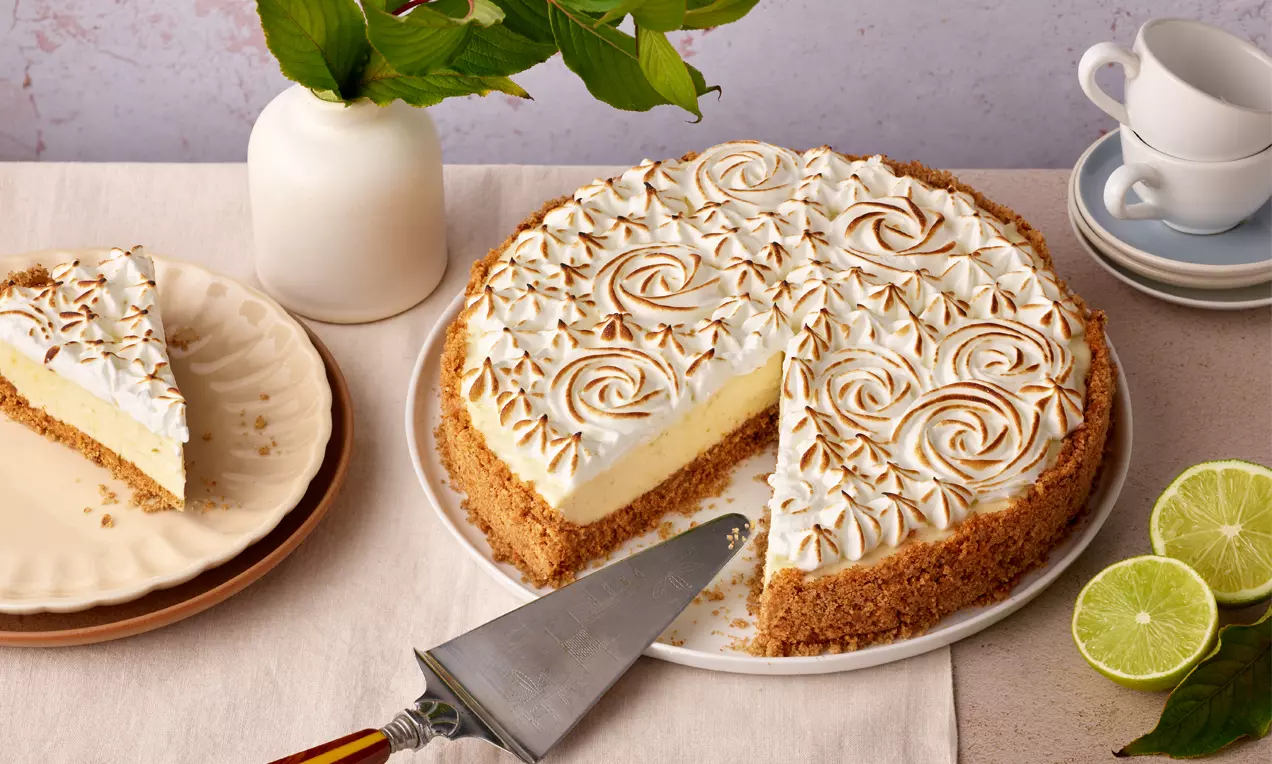 Schoko-Cheesecake mit goldbraunem Keksboden und heller Creme, dekoriert mit gerösteten Baiser-Rosetten auf weißer Platte