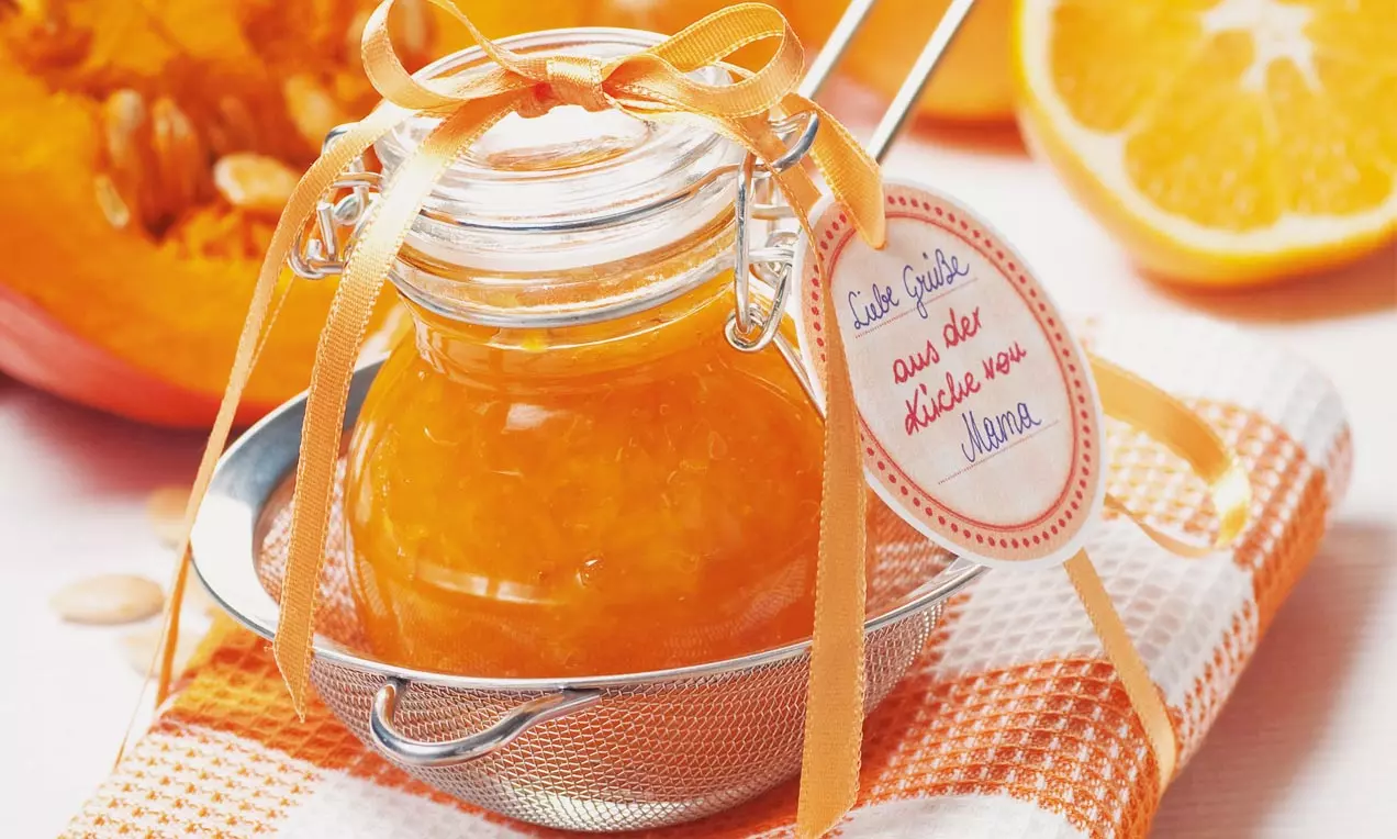 Glas mit leuchtend orangefarbener Kürbis-Orangenmarmelade, dekoriert mit orangefarbenen Schleifen auf weiß-orange kariertem Stoff
