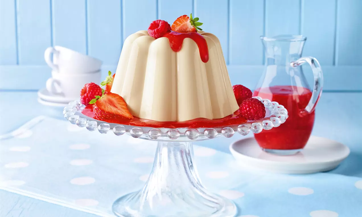 Marzipanfarbener Pudding in Gugelhupfform mit glänzender Erdbeer-Himbeersoße, dekoriert mit Erdbeeren und Himbeeren auf einer Glasplatte