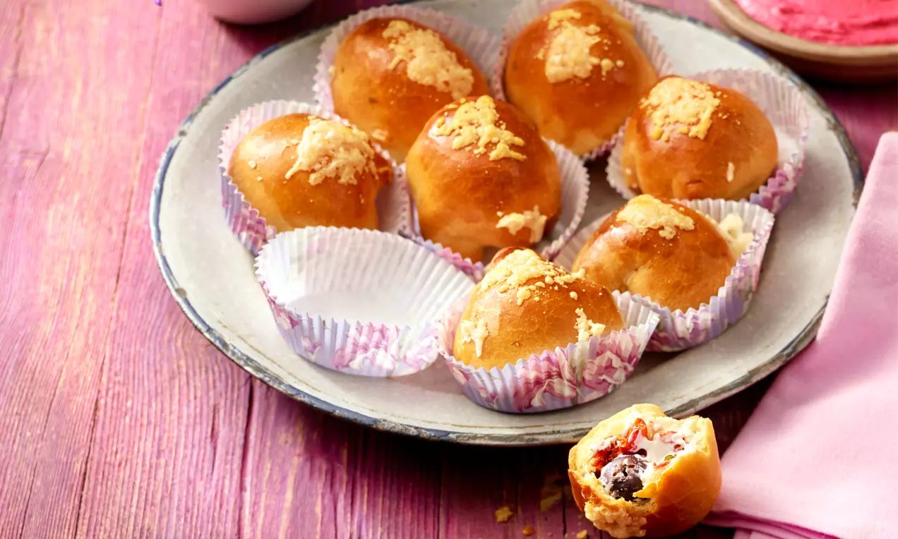 Goldbraune Pizzabällchen mit glatter Oberfläche und knusprigen Käsekrümeln, in gemusterten Papierförmchen auf einem Teller angeordnet
