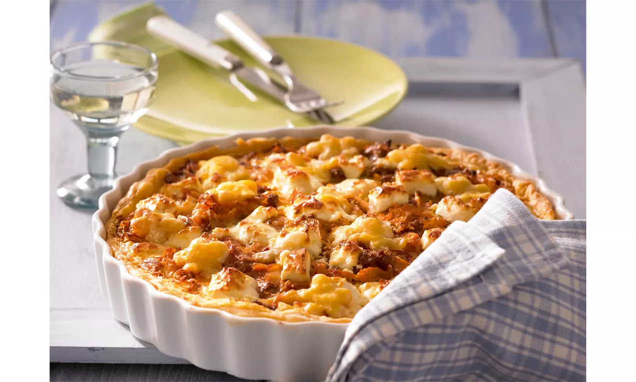 Goldbraune Weißkohl-Blätterteig-Quiche mit blättriger Kruste in weißer Tarteform, daneben kariertes Küchentuch und gedeckter Tisch