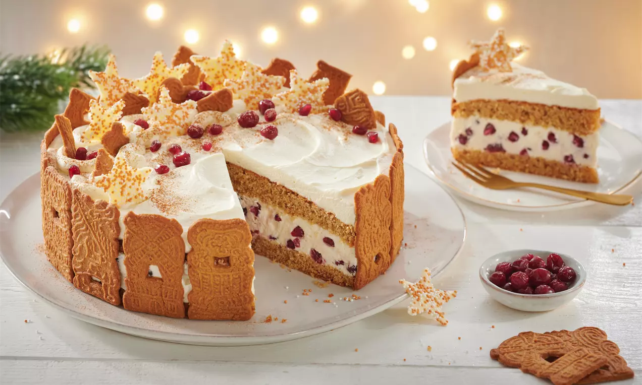Käse-Sahne-Torte mit goldbraunem Spekulatiusrand, weißer Cremehaube, roten Beeren und dekorativen Sternen auf einem weißen Teller