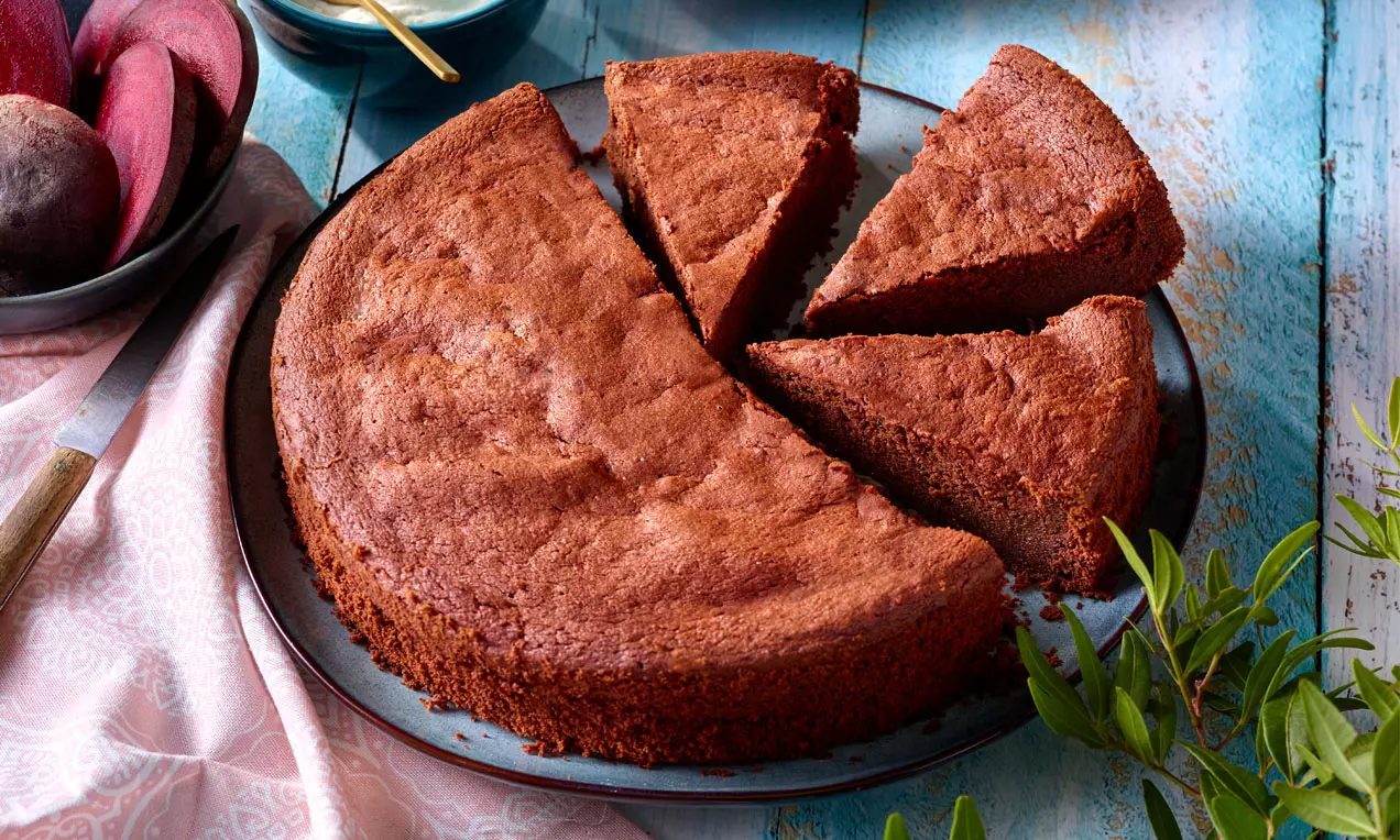 Dunkler, rundlicher Schoko-Rote-Bete-Kuchen mit saftiger Textur, in mehrere Stücke geteilt auf schwarzem Teller mit grüner Dekoration