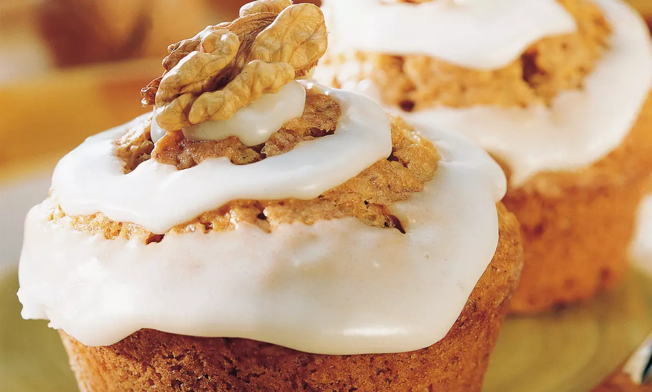 Goldbraune Walnuss-Bananen-Muffins mit glänzend weißer Glasur und dekorativen Walnusshälften auf grünlichem Teller angerichtet