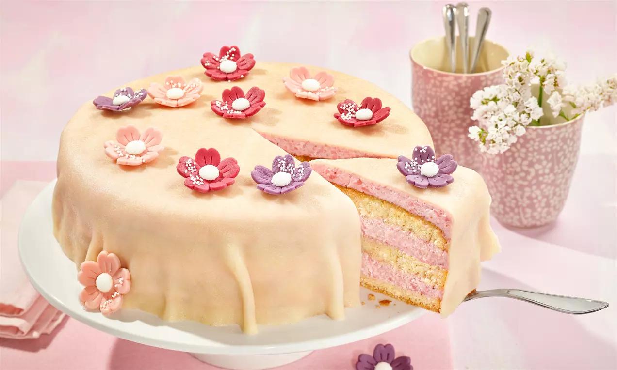 Anschnitt einer Torte mit pastellfarbenem Marzipanüberzug, rosa Schichten, verziert mit filigranen Zuckerblüten auf einer weißen Tortenplatte