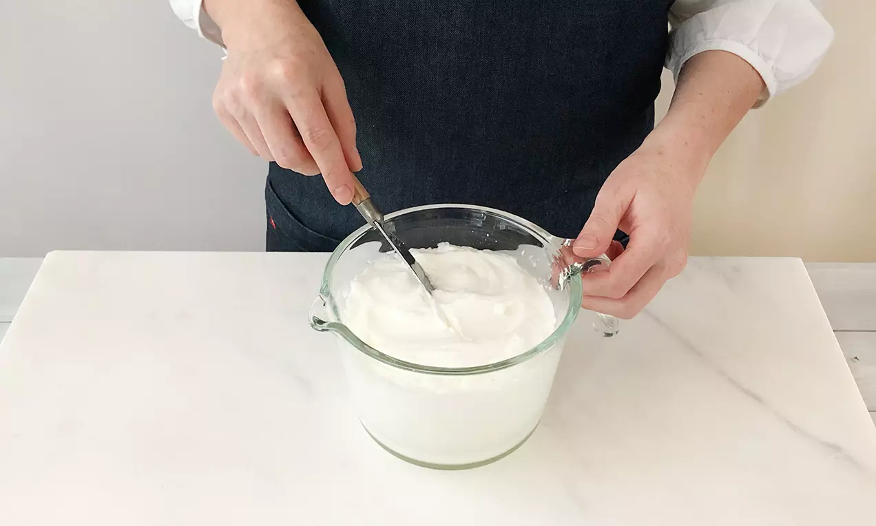 Schneeweißes, luftiges Eiweiß in einer Glasrührschüssel auf heller Arbeitsfläche, von Hand mit einem Messerschnitt geprüft