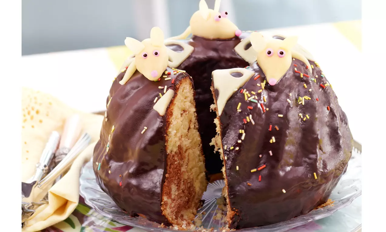 Marmorkuchen mit glänzender Schokoladenglasur, bunten Streuseln und weißen Mäuse-Dekoren, angeschnitten auf einer Glasplatte