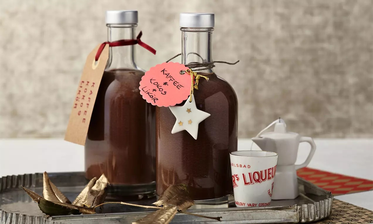 Zwei klare Glasflaschen mit braunem Kaffee-Kokos-Likör, verziert mit Anhängern und Sternendekoration, auf einem silbernen Tablett mit kleinen Beigaben