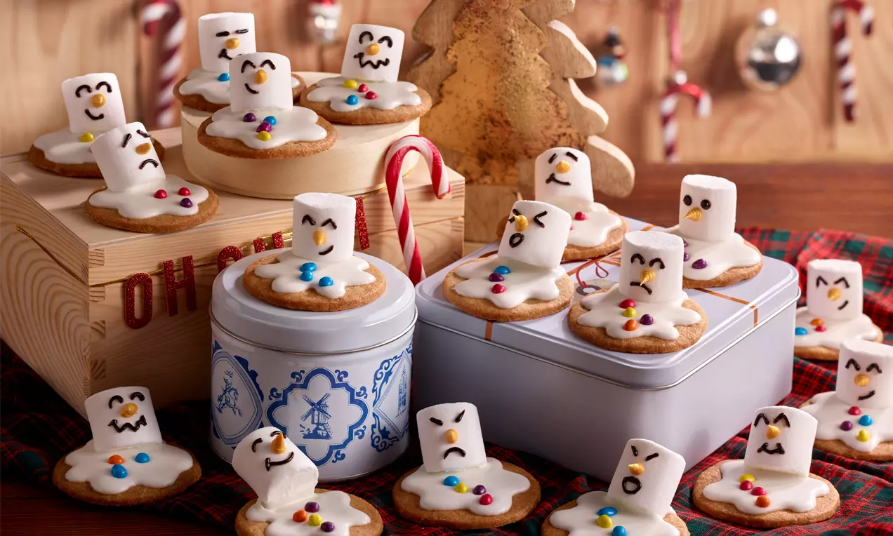Schneemann-Kekse mit geschmolzener weißer Glasur, Marshmallow-Kopf und bunten Zuckerstreuseln auf Dosen und Holzrahmen arrangiert