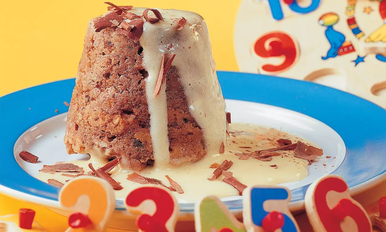 Zylinderförmiger Schokokuchen mit dunklen Krümeln in fließender Vanillesoße, garniert mit Schokoladenraspeln auf einem weißen Teller
