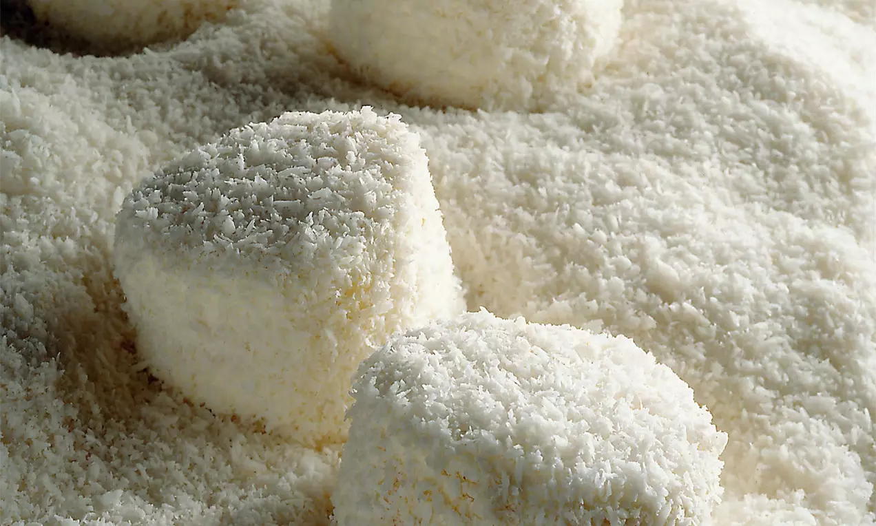 Runde, zarte Gebäckstücke mit flauschiger Kokosraspelschicht auf einer flächig bestreuten weißen Kokosunterlage